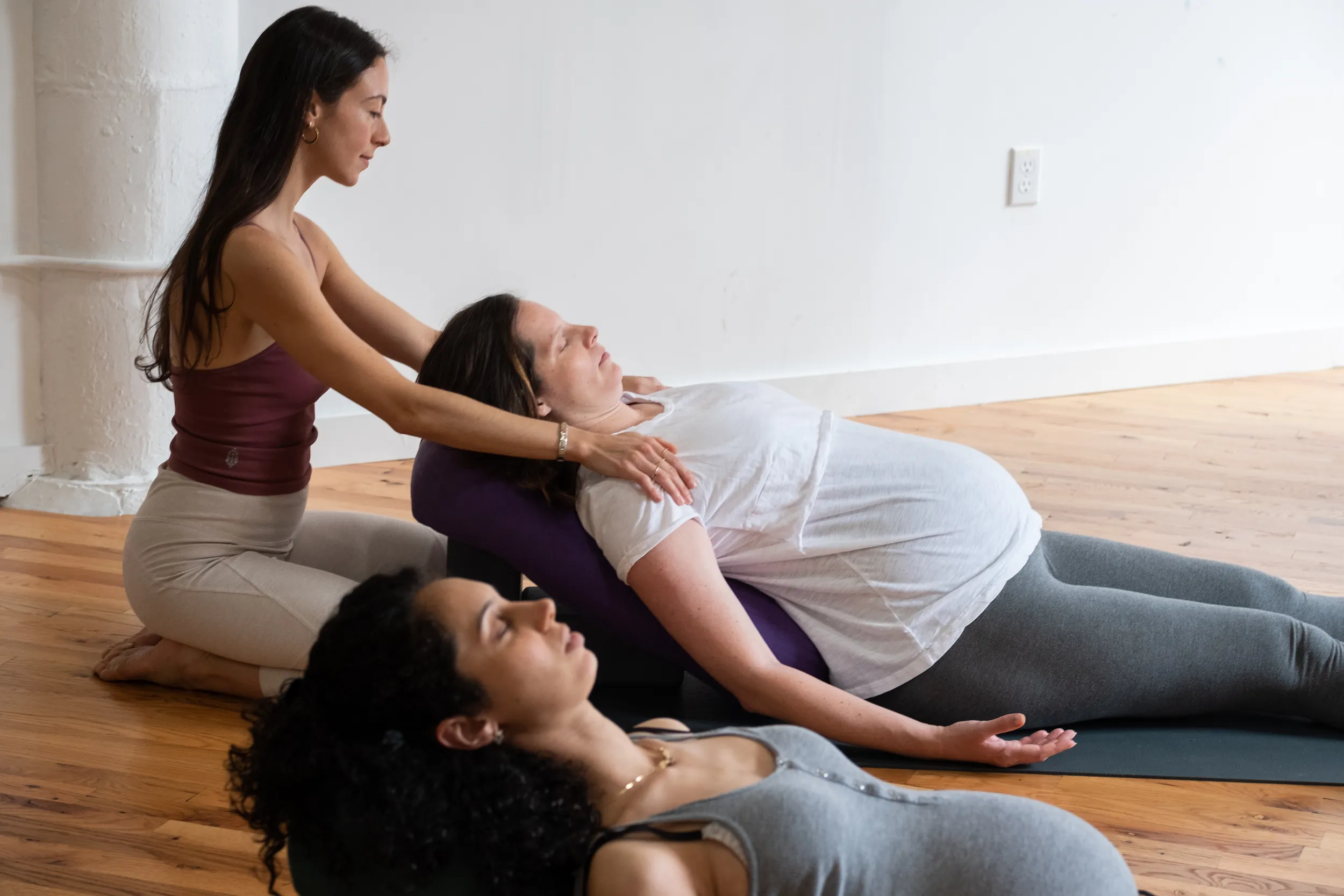 A prenatal yoga teacher supporting a pregnant student in a reclined restorative pose at Tangerine Yoga in Brooklyn