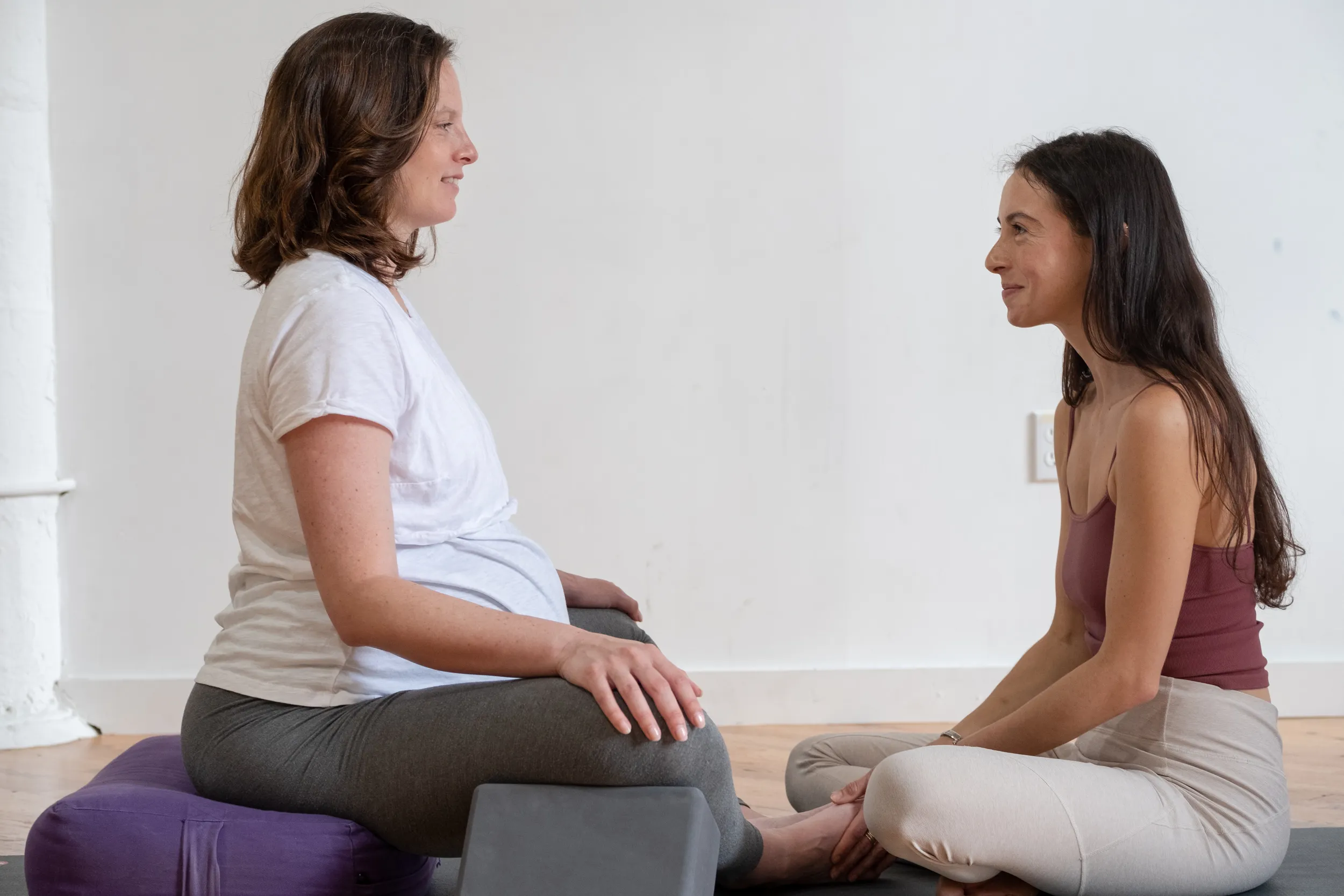 A prenatal yoga teacher talking with a pregnant student during class at Tangerine Yoga in Brooklyn